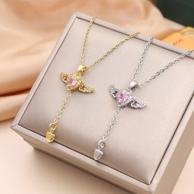 Two Moving Cupid Heart angel wings necklaces with crystal, one gold and one silver, displayed in a gift box on a beige fabric background